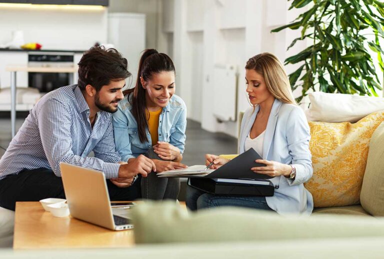 A person reviewing their car insurance policy with paperwork and a laptop at a kitchen table.