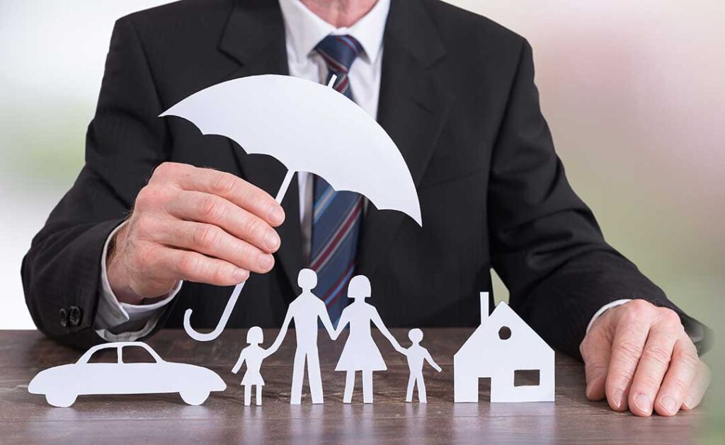 A couple reviews umbrella insurance documents beside a laptop and homeowners policy at a kitchen table.